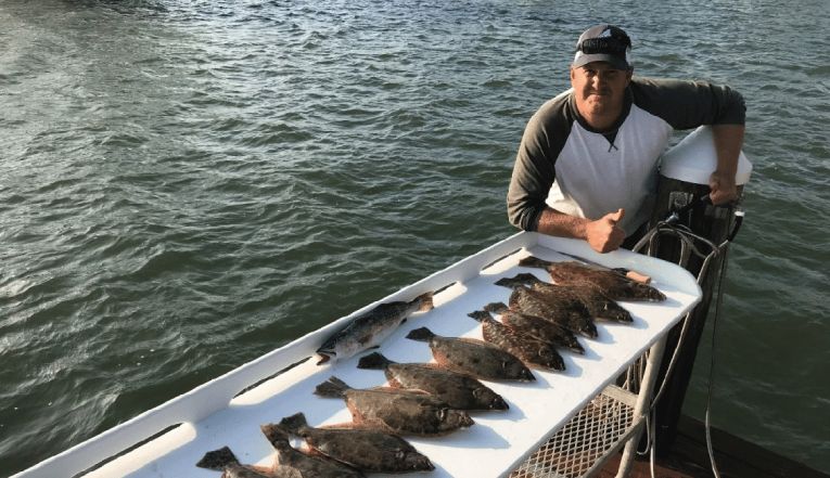 A man sitting with pile of fish on the table.