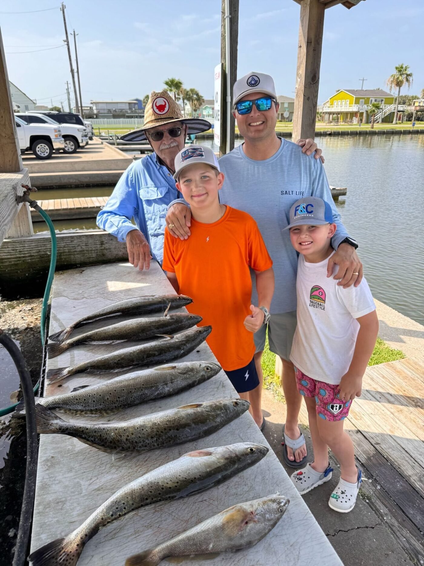 Grandfather, father, and two kids proudly pose with their impressive speckled trout catch on a dock during a Frenzy fishing trip