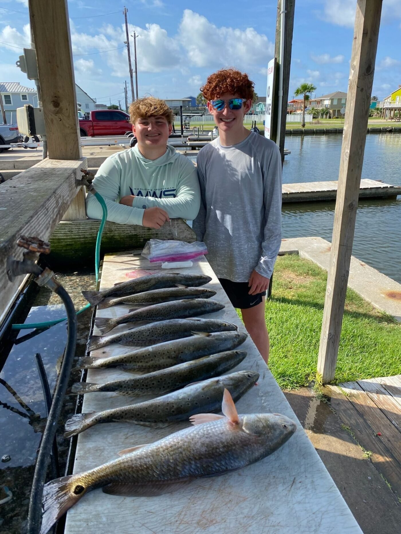 Two teenage anglers smiling next to a table full of speckled trout after a successful morning charter with Frenzy Guide Service