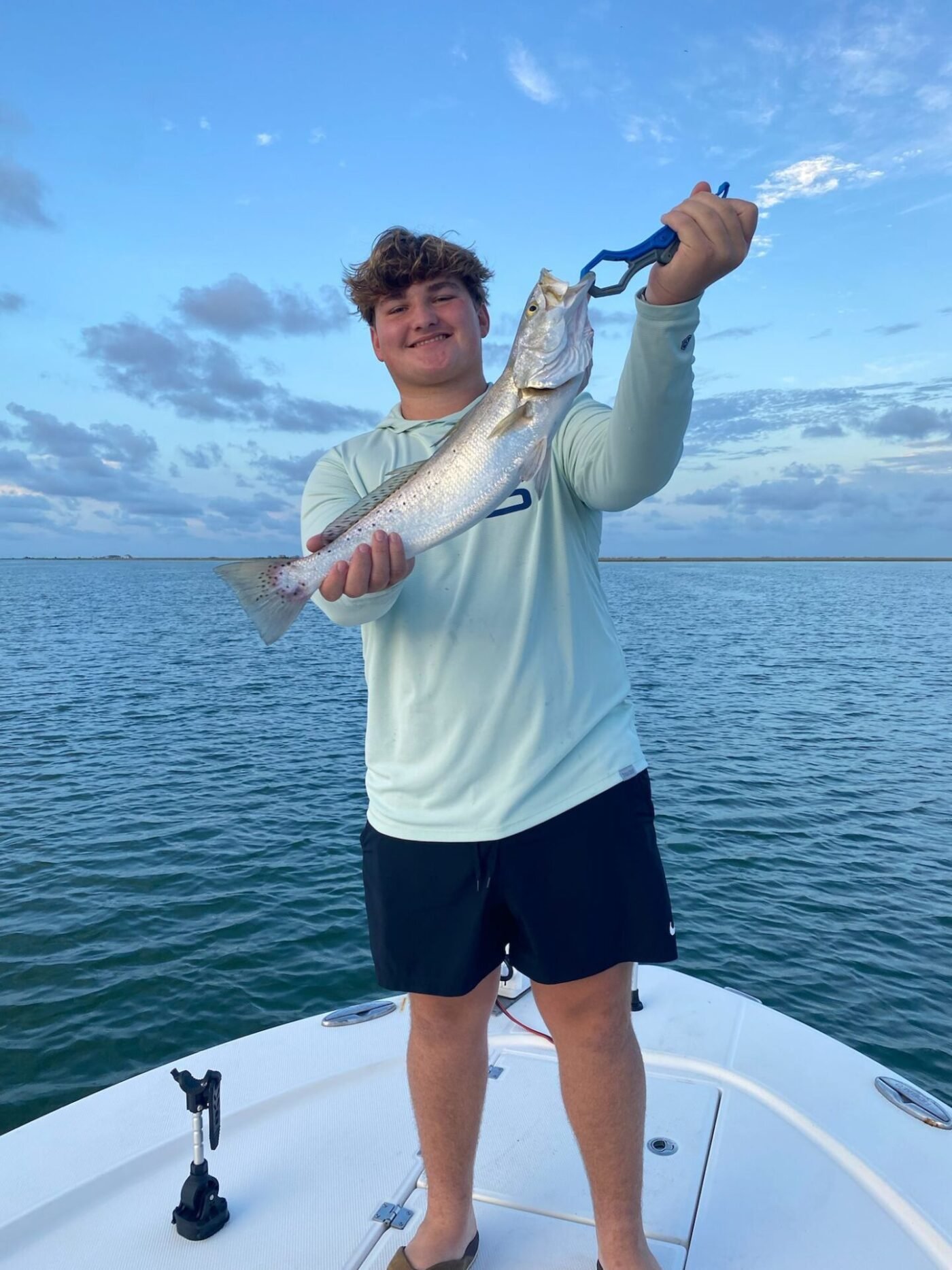 Smiling teenager proudly holding a freshly caught speckled trout on the front deck of a boat during a calm morning charter trip